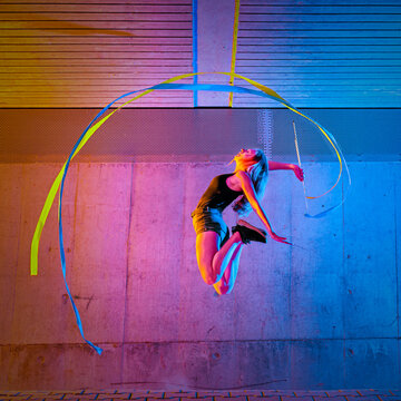 Woman jumping while spinning ribbon against wall