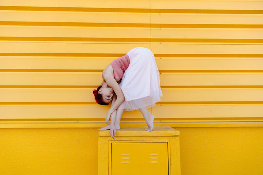 Ballerina bending while dancing on seat against yellow wall