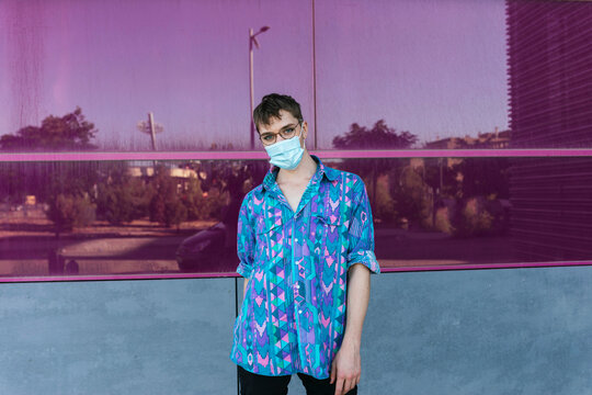 Non-binary person wearing face mask while standing against pink glass wall