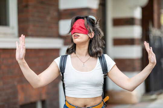 Young woman wearing red face mask on eye gesturing while standing in city
