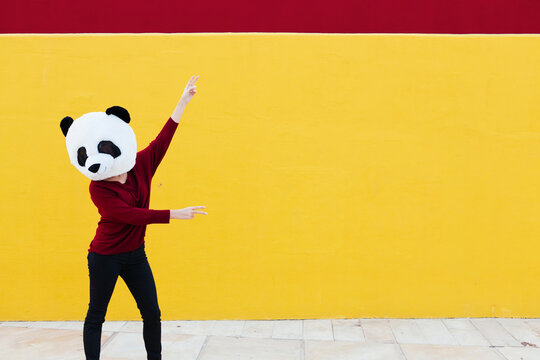 Woman wearing panda mask while dancing against yellow wall