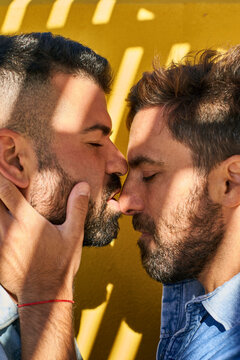 Gay couple doing romance while standing against yellow wall