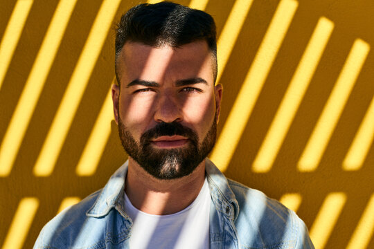 Young man with shadow on face standing against yellow wall outdoors