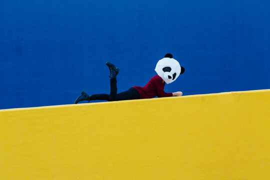 Woman wearing panda mask while lying down on yellow wall
