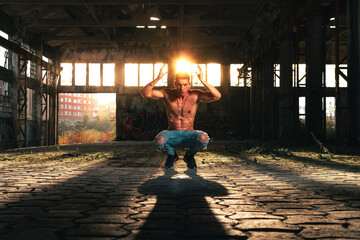 Fitness man posing in a ruined industry pavillion with the sunlight at the back.