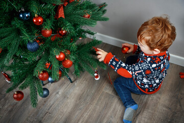 A child with a Christmas tree. A little blond boy  reaches for the toy on a beautiful green Christmas tree. Christmas photo