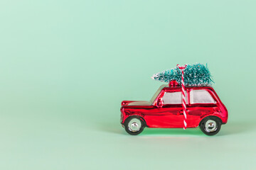 Red toy car with christmas tree decoration on turquoise background. Christmas, New Year holiday celebration concept 