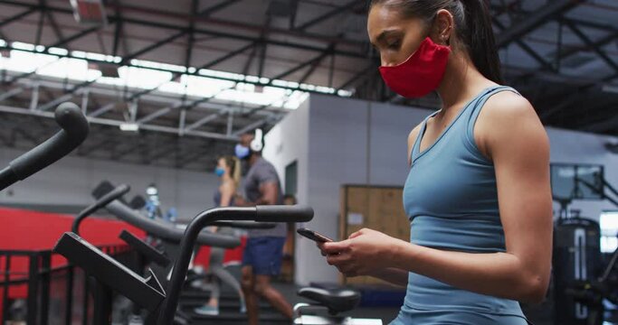 Mixed race woman wearing face mask using smartphone at gym