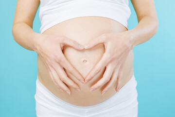 Woman standing and touching with hands her naked big belly. Isolated on blue background. Closeup of pregnant belly.