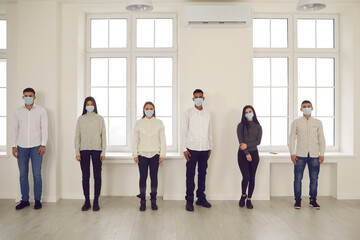 Young diverse people in face masks standing in the office, keeping social distance
