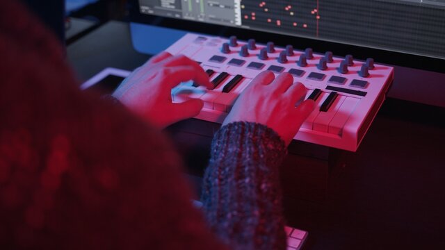 Recording music notes, playing electronic keyboard, midi keys in music sequencer. Hands and midi controller on the table with neon lights, man composing music in night