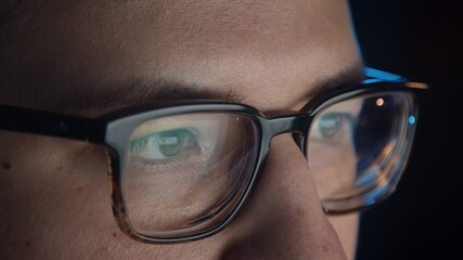Macro shot of man eyes in eyeglasses in front of the computer, gimbal shot in home office, concentrated look. Young man sitting at home working alone at night