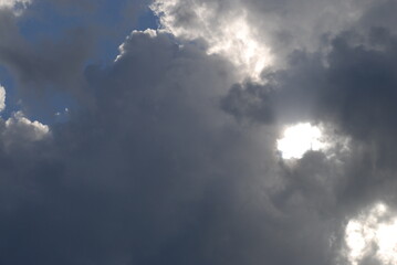 A formidable cloud with three bright gaps.
Summer sunny day. A formidable cloud floats across the sky from above, white from below, dark gray. In the dark cloud there are three white skylights from th