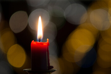 Burning candle on black background with bokeh. Christian christmas concept..