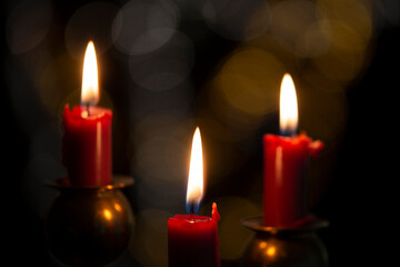 Burning candle on black background with bokeh. Christian Christmas concept.
