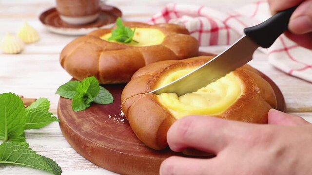 Sour cream bun cut with knife with mint leaves on a cutting board and linen textile. Side view, close up, selective focus.