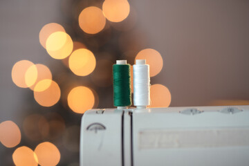 A close-up shot of two sewing threads, green and white, on the sewing machine and a Christmas tree on the background