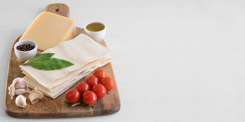 Ingredients for cooking Italian lasagna on wood cutting board stock photo. Ingredients: lasagna sheets, basil, cherry tomatoes, garlic, pepper, oil, wood cutting board.