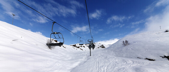 Fototapeta na wymiar Panoramic view on chair-lift and snowy off-piste slope on ski resort at sun winter day
