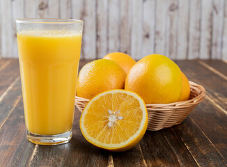 Orange juice with oranges in a basket and cut fruit over wooden table