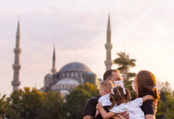Obraz premium Portrait of happy tourist family in mask in front of Blue Mosque Istanbul, Turkey. Tourism back to Turkey after covid-19 lockdown. Cute mother, father, daughter, son travel together, posing for photo