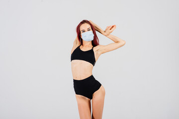 Fototapeta na wymiar Female dancer in the styles of strip-plastic and pole dance with face mask on light background.