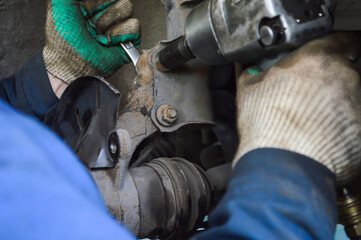 Car mechanic unscrew the lower mount of the front shock absorber of the car