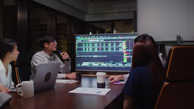 Young Asian businessman lead group of business financial team in strategic meeting presentation, work late night in office. Marketing strategy analysis, stock market trading, or corporate teamwork