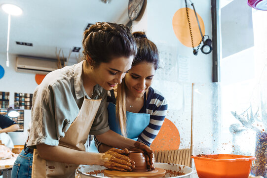 Positive women smiling while creating jug with pottery wheel in workshop