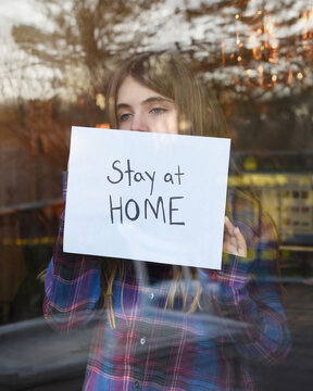 Girl Holding A Stay At Home Sign In Window
