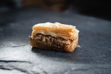 primer plano macro de baklava pastel típico y tradicional turco masa hojaldrada y nuez y pistacho triturado con miel y almíbar de azúcar sobre plato de piedra laja negra