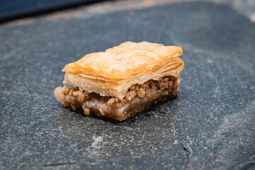 primer plano macro de baklava pastel típico y tradicional turco masa hojaldrada y nuez y pistacho triturado con miel y almíbar de azúcar sobre plato de piedra laja negra