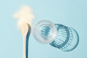 A spoon with collagen and a glass of water on blue  background with a copy of space.