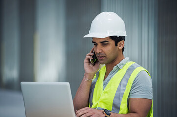 Indian worker using laptop and cell phone in warehouse