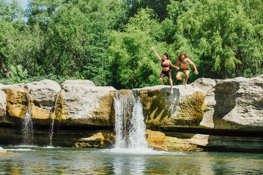 Caucasian couple jumping off rocks near waterfalls