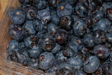 Blaubeeren in einer Kunststoffverpackung auf einem Holzbrett.