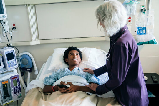 Doctor comforting boy in hospital bed holding cell phone