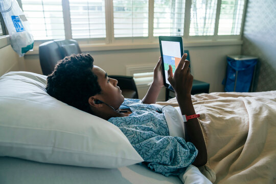 Black boy in hospital bed listening to digital tablet