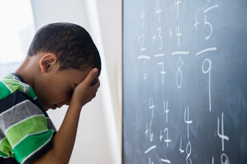 Mixed race boy doing math problems at board in class