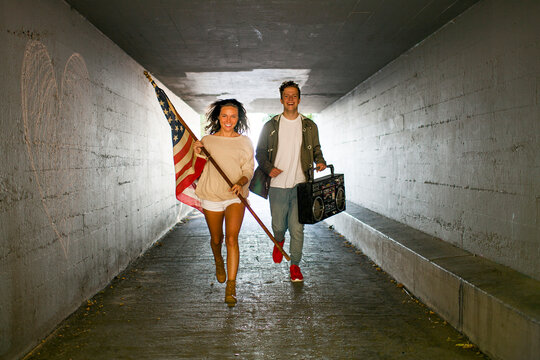 Caucasian couple carrying American flag and boom box in tunnel
