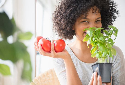Smiling woman with tomatoes smelling plant