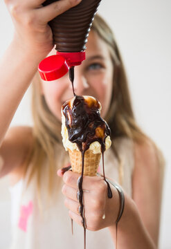 Messy Caucasian girl pouring chocolate syrup on ice cream cone
