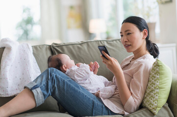 Asian mother using cell phone and holding baby in living room