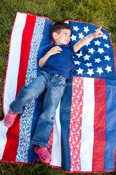 Mixed race boy pointing up on American flag blanket on grass