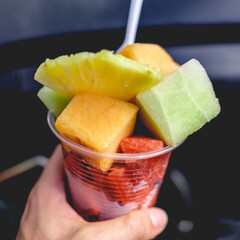 Hand holding a cup of fruit salad (melon, watermelon, pineapple)