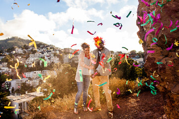 Couple throwing confetti on hill overlooking cityscape