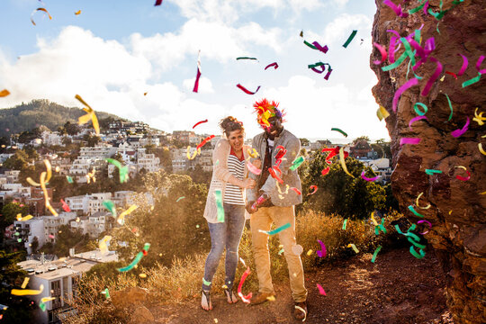 Couple throwing confetti on hill overlooking cityscape