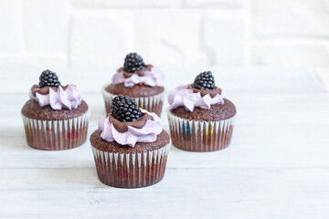 Delicious cupcakes with lilac cream and blackberries on a light background.