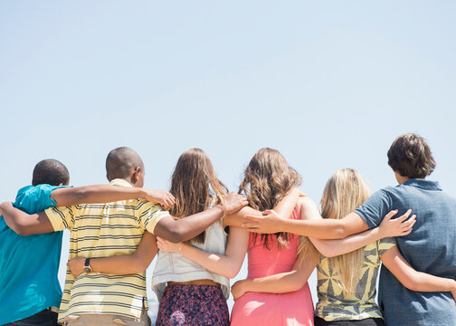 Rear view of teenagers hugging under blue sky