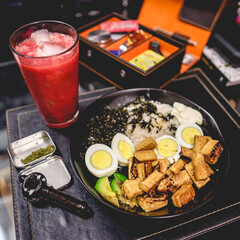 Awesome homemade dinner with fruit juice, a plate of fried tofu, rice, algae, boiled eggs, avocado and rice, and a pipe and box with marijuana